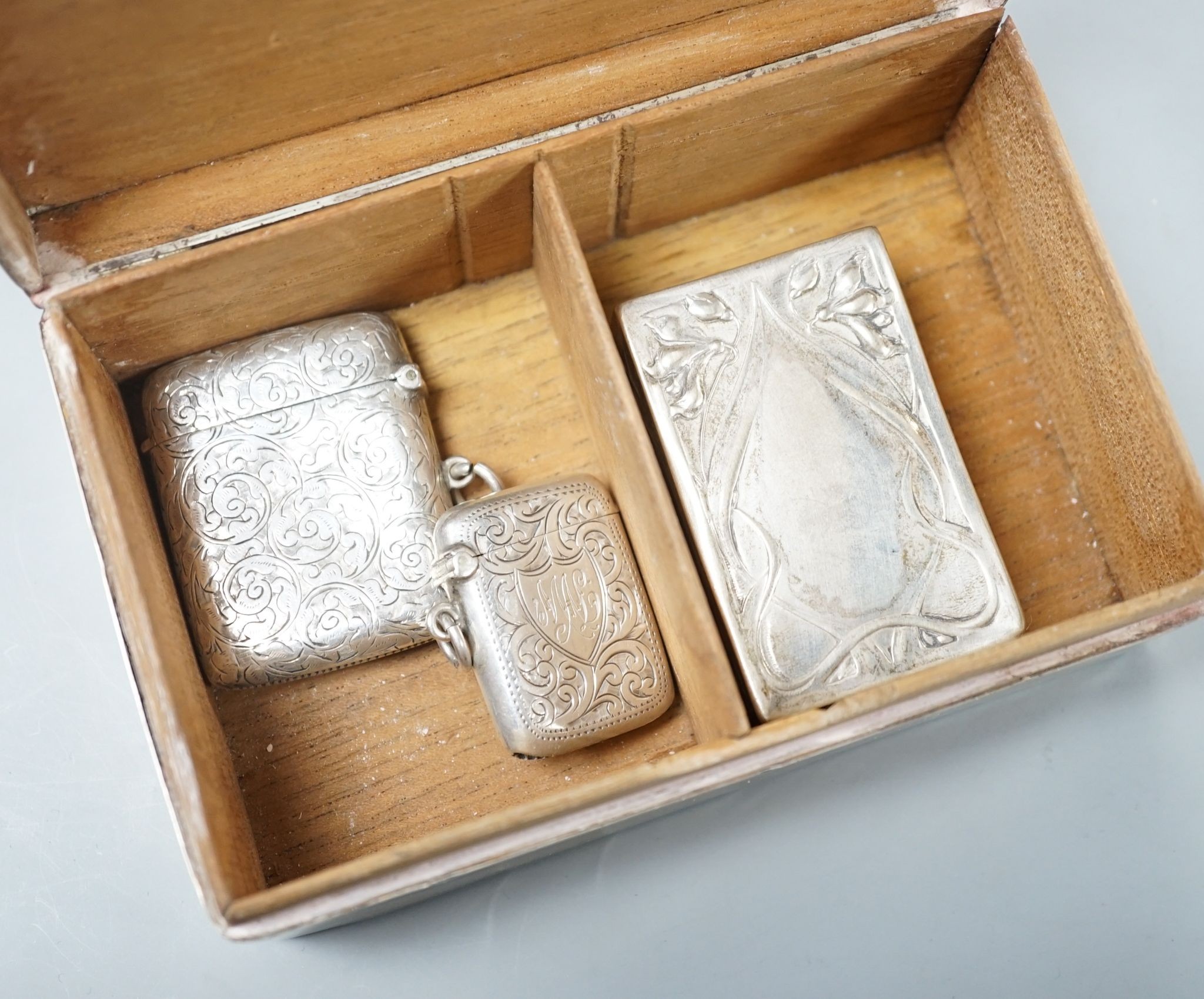 A silver mounted cigarette box, two silver vestas and a silver matchbox sleeve.